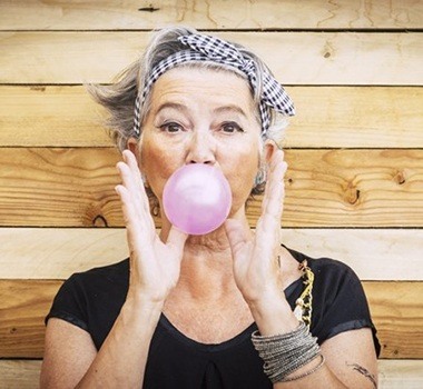 elderly woman blowing a bubble with pink chewing gum