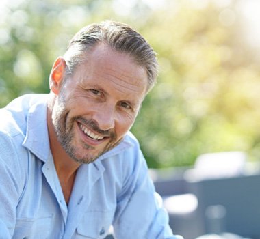 Man in light blue shirt sitting outside and smiling