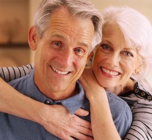  Older couple smiling with woman’s arms around man 