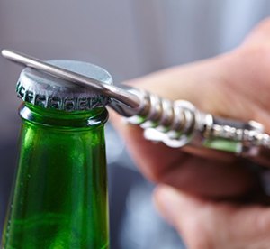 person using a bottle opener to crack open a green glass bottle 