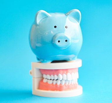 Piggy bank atop model teeth representing the cost of veneers in Landrum