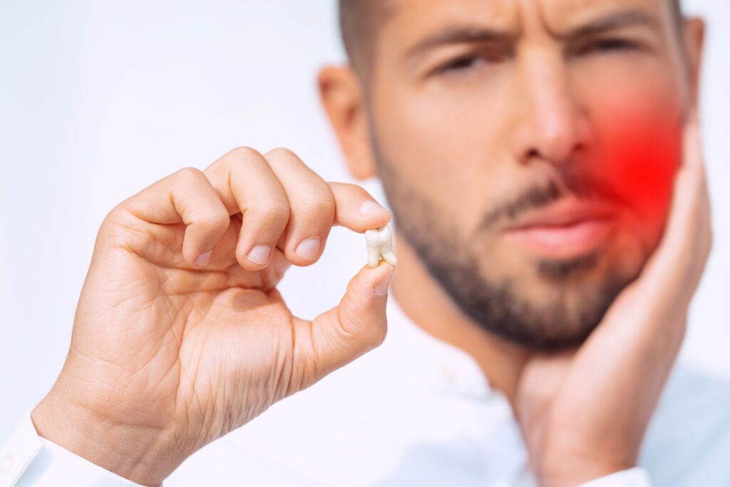 Man holding swollen jaw with one hand and extracted tooth in the other