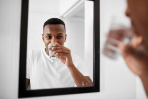 Man sipping small glass of salt water in front of bathroom mirror